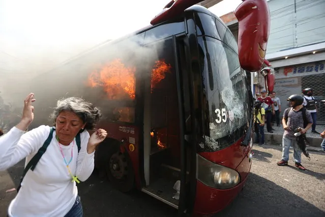 A woman moves away from the flames of a burning bus after it was pushed away during clashes with the Bolivarian National Guard in Urena, Venezuela, near the border with Colombia, Saturday, February 23, 2019. (Photo by Fernando Llano/AP Photo)