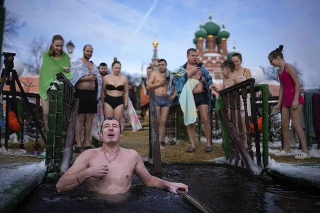 A man crosses himself as other people lineup to bath into the icy water on Epiphany during a traditional Epiphany at the Great Palace Pond with the Church of the Holy Trinity in Ostankino in the background in Moscow, Russia, on Friday, January 19, 2024. Across Russia, the devout and the daring are observing the Orthodox Christian feast day of Epiphany by immersing themselves in frigid water through holes cut through the ice of lakes and rivers. Epiphany celebrates the revelation of Jesus Christ as the incarnation of God through his baptism in the River Jordan. (Photo by Alexander Zemlianichenko/AP Photo)