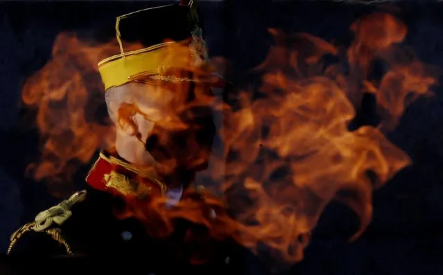 A Romanian honor guard soldier wearing a protective mask stands at attention, as seen through the eternal flame, at the Unknown Soldier Memorial, during the Romanian Army Day celebration, in Bucharest, Romania, 25 October 2021. The Armed Forces Day in Romania is marked to commemorate retaking Carei, the last Romanian city under joint German-Hungarian occupation on 25 October 1944. (Photo by Robert Ghement/EPA/EFE)