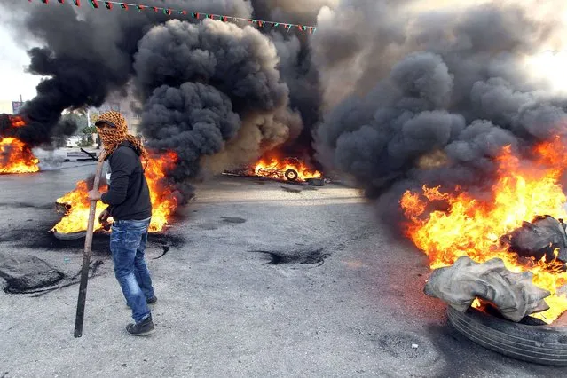 A protestor walks in front of burning tyres as they block a street in Libya's second city of Benghazi on February 26, 2014 after the killings of two policemen. The fatal shootings of the two officers – one serving, one retired – came just a day after the UN mission in Libya voiced “deep concern” over the near-daily violence plaguing the North African country, particularly the east. (Photo by Abdullah Doma/AFP Photo)