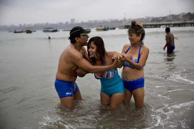 In this May 8, 2015 photo, friends help Gisela Sanchez who suffers rheumatoid arthritis walk in the water off Fishermen's Beach in Lima, Peru. “The sand calms the inflammation in my joints and the sea gives me tranquility”, said Sanchez, who traveled here from Patapo, a village at the foot of the Andes mountains about 700 kilometers (1,690 miles) north of Lima. (Photo by Rodrigo Abd/AP Photo)