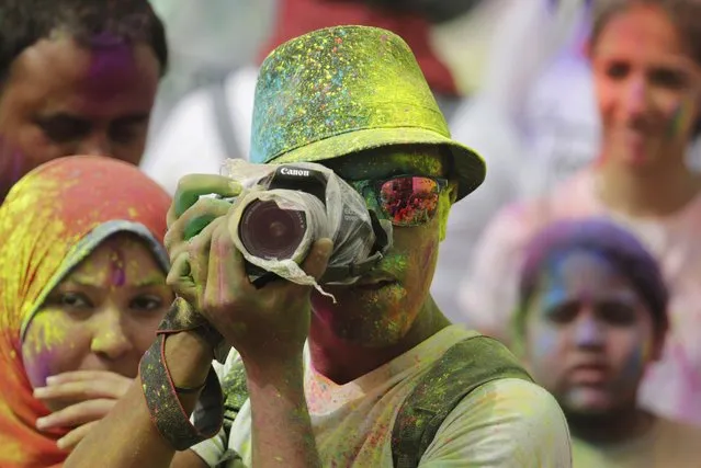 A photographer covers his camera from colored paint as he documents the Festival of Colors organized by the Indian Cultural Center in Cairo, Egypt, Friday, April 8, 2016. Throwing color is a traditional Hindu way to enthusiastically embrace the changing season and celebrating spring. (Photo by Amr Nabil/AP Photo)