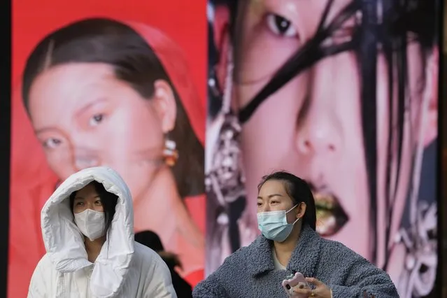 Women wearing masks walk past ads featuring models for make up products in Beijing, China, Tuesday, December 28, 2021. Advertisements featuring some Chinese models have sparked feuding in China over whether their appearance and makeup are perpetuating harmful stereotypes of Asians. (Photo by Ng Han Guan/AP Photo)