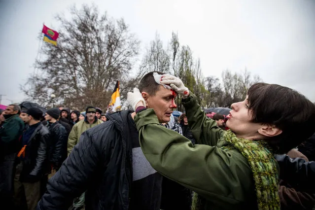 A Ukrainian woman helps an injured man during the clashes between Ukrainian activists protesting the occupiation of local government buildings by pro-Russia separatists, and Russia's supporters on April 13, 2014 in the Ukrainian city of Zaporizhia. (Photo by Maxim Scherbina/Getty Images/Anadolu Agency)