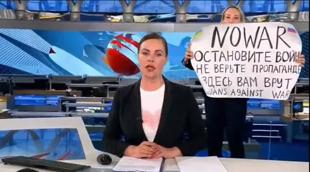 This video grab taken on March 15, 2022 shows Russian Channel One editor Marina Ovsyannikova holds a poster reading “ Stop the war. Don't believe the propaganda. Here they are lying to you” during on-air TV studio by news anchor Yekaterina Andreyeva , Russia's most-watched evening news broadcast, in Moscow on March 14, 2022 . As a news anchor Yekaterina Andreyeva launched into an item about relations with Belarus, Marina Ovsyannikova, who wore a dark formal suit, burst into view, holding up a hand-written poster saying “No War” in English. (Photo by Handout/AFP Photo)