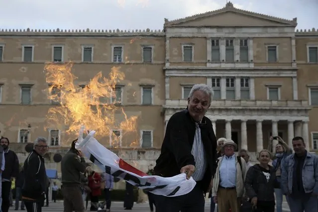 A demonstrator burns a party flag or Syriza ruling party outside the parliament building as Greek lawmakers vote on the latest round of austerity Greece has agreed with its lenders, in Athens, Greece, May 18, 2017. (Photo by Costas Baltas/Reuters)