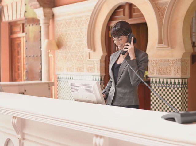 Hotel receptionist talking on telephone. (Photo by Robert Daly/Getty Images)