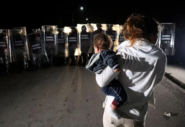 A migrant woman carries her baby as members of the National Guard block the street during an operation to dissolve a caravan of migrants and asylum seekers from Central America and the Caribbean as they try to make their way to the U.S., in Huixtla, Chiapas, Mexico on September 5, 2021. (Photo by Jose Torres/Reuters)