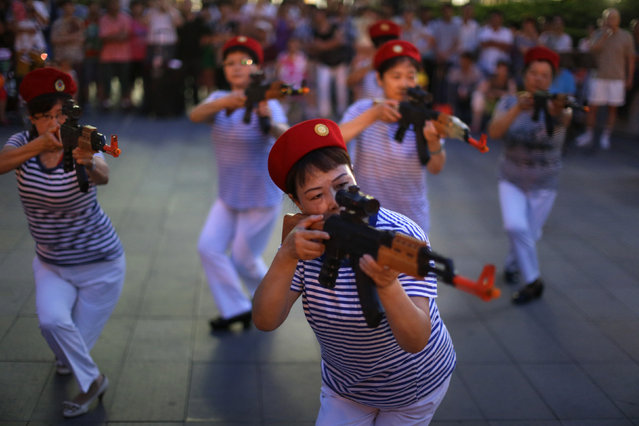 Chinese women holding toy guns dance for a revolutionary song during their daily exercise at a square outside a shopping mall in Beijing, June 29, 2014. About 30 local residents formed this “Nanguan” art group that enjoys performing to revolutionary songs and dance performances as part of their daily fitness activities at night. (Photo by Jason Lee/Reuters)