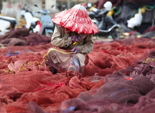 A fisherwoman repairs the fishing nets at a fishing port during the annual summer fishing ban, which covers the Bohai Sea, the Yellow Sea, the East China Sea, and the waters north of 12 degrees north latitude in the South China Sea, on June 8, 2022 in Wenling, Taizhou City, Zhejiang Province of China. (Photo by Liu Zhenqing/VCG via Getty Images)