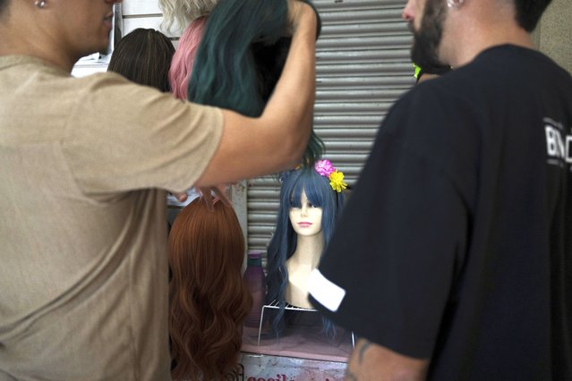 News anchor Guillermo Barraza and his partner Francisco check out the wigs at a bazaar in Mexico City, Saturday, October 28, 2023. Growing up gay in the hyper-conservative northern city of Culiacán, Sinaloa, Barraza never saw gay characters he identified with on a deeper level. (Photo by Aurea Del Rosario/AP Photo)