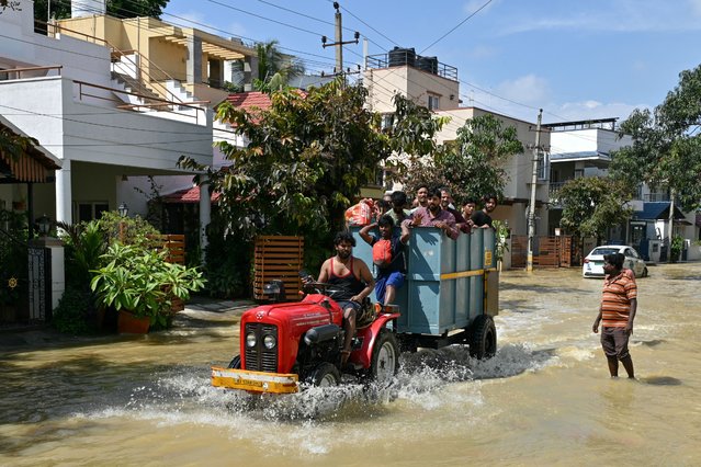 Workers commute through a flooded road following heavy rainfall in Bengaluru on October 21, 2024. (Photo by Idrees Mohammed/AFP Photo)