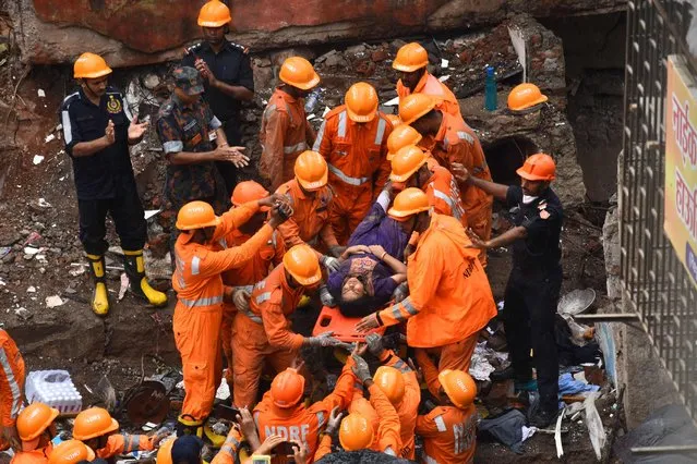 Rescue workers cheer as a survivor is brought out alive on a stretcher from the debris of a collapsed building in Mumbai on June 28, 2022. (Photo by Imtiyak Shaikh/AFP Photo)
