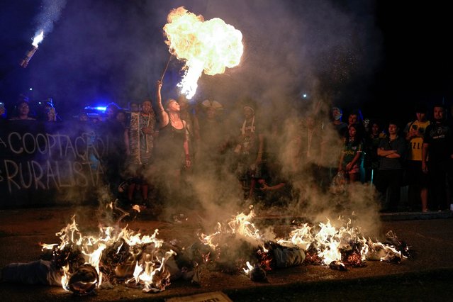 A demonstrator spits fire next to burning puppets representing politicians as she joins Indigenous people and environmental activists in a climate protest in Sao Paulo, Sunday, September 22, 2024. (Photo by Andre Penner/AP Photo)