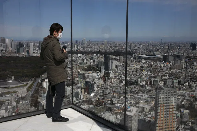 A man wearing a mask views Tokyo's skyline from Shibuya Sky observation deck as the New National Stadium, a venue for the opening and closing ceremonies at the Tokyo 2020 Olympics, is visible in the distance in Tokyo, Tuesday, March 3, 2020. The Japanese government has indicated it sees the next couple of weeks as crucial to containing the spread of COVID-19, which began in China late last year. (Photo by Jae C. Hong/AP Photo)
