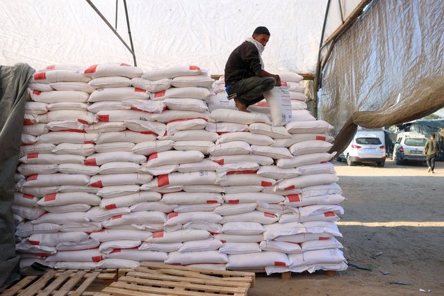 A Palestinian worker rests on a stack of flour at an aid distribution centre in the southern Gaza Strip city of Khan Yunis on December 3, 2024, amid the ongoing war between Israel and the Palestinian Hamas movement. (Photo by Bashar Taleb/AFP Photo)