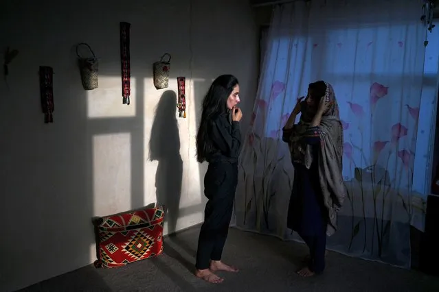 In this photograph taken on May 28, 2022, an Afghan female presenter with news network 1TV, Lima Spesaly (C) speaks with her sister Banafsha Wahab inside their residence in Kabul. After initially defying the Taliban order to cover their faces on air, Afghan women television presenters are broadcasting news and other programmes wearing masks. Spesaly, said it was difficult to work like this for hours but vowed to fight for her rights and of other Afghan women that are being increasingly crushed by the hardline Islamist rulers. (Photo by Wakil Kohsar/AFP Photo)
