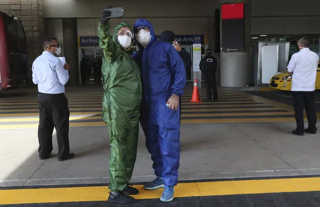 A couple decked out in full protection suits and wearing masks against the spread of the new coronavirus, take a selfie while waiting for the arrival of their son in one of the firsts international flights from United States, outside the Mariscal Sucre airport, in Quito, Ecuador, Thursday, June 4, 2020. The airport's waiting area was closed to prevent agglomerations amid the COVID-19 pandemic. (Photo by Dolores Ochoa/AP Photo)