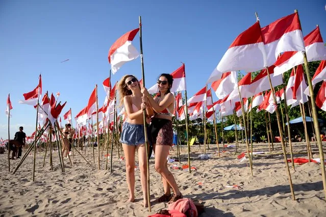 Foreign tourists hold an Indonesian national flag during a parade a day before Indonesia Independence day at Kuta on Indonesia's resort island of Bali on August 16, 2016. (Photo by Sonny Tumbelaka/AFP Photo)