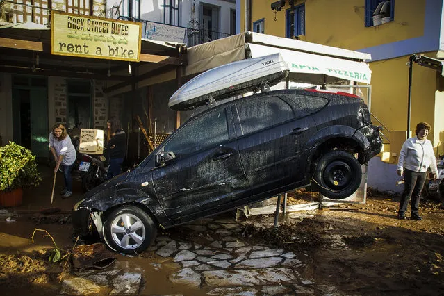 Staff at a car rental store clean up damage in front of a washed up vehicle following a powerful storm on the Greek island of Symi, on Tuesday, November 14, 2017. Authorities declared a state of emergency on the east Aegean Sea island after the storm caused extensive flooding, road damage, and power outages. (Photo by Argiris Madikos /Eurokinissi via AP Photo)