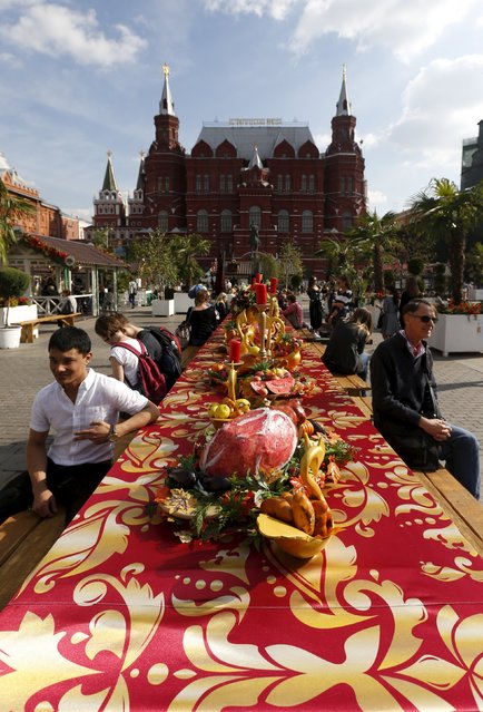 People sit at table with food models as the gastronomic festival “Moscow autumn” takes place near the Kremlin (R) and the State Historical Museum (L) in central Moscow, Russia, September 16, 2015. (Photo by Sergei Karpukhin/Reuters)