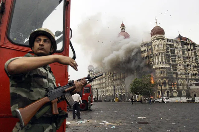 An Indian soldier takes cover as the Taj Mahal hotel burns during a gun battle between Indian military and militants inside the hotel in Mumbai, India, November 29, 2008. The three days of terror in Mumbai carried out by the Pakistan-based militant group Lashkar-e-Taiba left 166 people dead. (Photo by David Guttenfelder/AP Photo/File)
