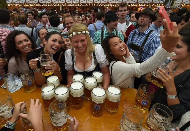 Visitors enjoy the atmosphere and take selfies as a waitress serves beer mugs during the opening of the Oktoberfest beer festival in a festival tent at the Theresienwiese in Munich, southern Germany, on September 17, 2016. The World's largest beer festival Oktoberfest will run until October 3, 2016. (Photo by Christof Stache/AFP Photo)