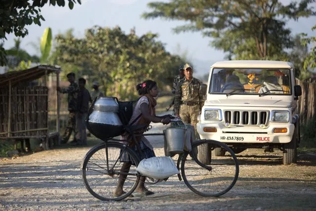 Indian policemen stand guard as an Indian tribal girl leaves for a relief shelter after her village was attacked by an indigenous separatist group, in Shamukjuli village in Sonitpur district of Indian eastern state of Assam, Wednesday, December 24, 2014. (Photo by Anupam Nath/AP Photo)