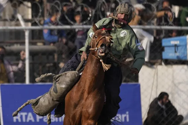 An Afghan horse rider carries a goat effigy, as he competes during a Buzkashi league match, in Kabul, Afghanistan, Sunday, February 27, 2022. Buzkashi is a popular traditional sport of Afghanistan in which horse-mounted players attempt to place a goat or calf carcass in a goal, nowadays an effigy is used instead of a carcass. During the first Taliban rule of Afghanistan Buzkashi was banned. (Photo by Hussein Malla/AP Photo)