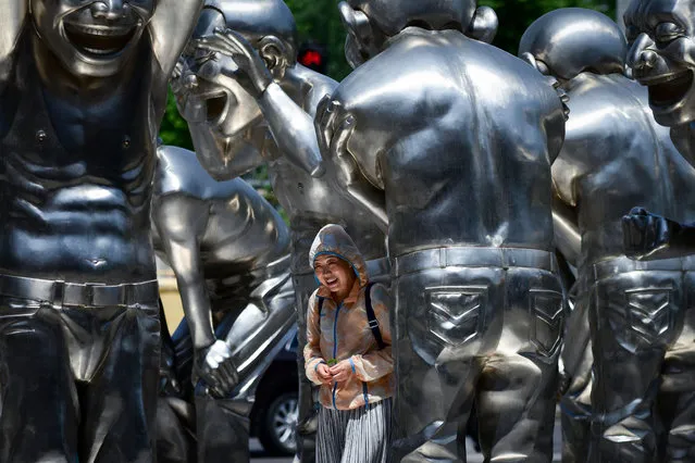 A woman walks past sculptures by Chinese artist Yue Minjun outside an art museum in Beijing on May 18, 2018. (Photo by Wang Zhao/AFP Photo)