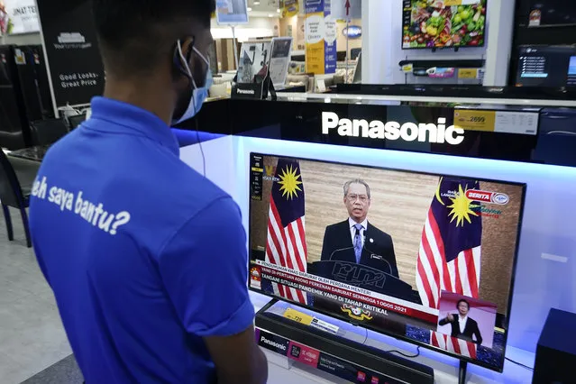 An electronic shop worker wearing a face mask watches a live broadcast of Malaysian Prime Minister Muhyiddin Yassin at a shopping outlet in Kuala Lumpur, Malaysia, Tuesday, January 12, 2021. Malaysia's king Tuesday approved a coronavirus emergency that will prorogue parliament and halt any bids to seek a general election in a political reprieve for embattled Muhyiddin. (Photo by Vincent Thian/AP Photo)