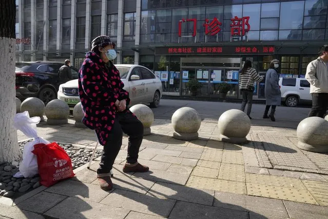 A resident wearing a mask sits outside the clinic entrance of the Hubei Provincial Hospital of Integrated Chinese and Western Medicine also known as the Hubei Province Xinhua Hospital where a World Health Organization team of researchers arrive on its first field trip in Wuhan in central China's Hubei province on Friday, January 29, 2021. The World Health Organization team of researchers emerged from their hotel Thursday for the first time since their arrival in the central Chinese city of Wuhan to start searching for clues into the origins of the COVID-19 pandemic. (Photo by Ng Han Guan/AP Photo)