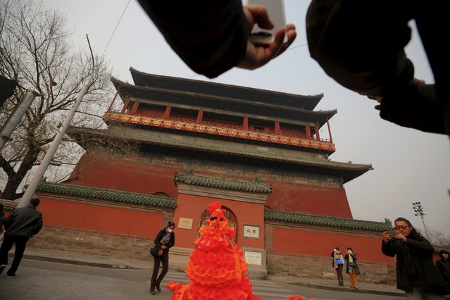 Passers-by take pictures of Chinese artist Kong Ning in her costume made of hundreds of orange plastic blowing horns during her art performance raising awareness of the hazardous smog in front of the Drum tower in a historical part of Beijing on a very polluted day December 7, 2015. (Photo by Damir Sagolj/Reuters)