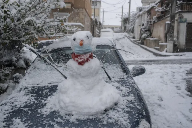 A snow man wearing a face mask stands on a car in Athens, on Tuesday, February 16, 2021. Unusually heavy snowfall has blanketed central Athens, with authorities warning residents particularly in the Greek capital's northern and eastern suburbs to avoid leaving their homes. (Photo by Petros Giannakouris/AP Photo)