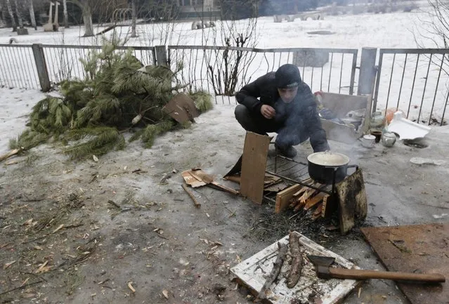 A man boils water on an open fire outside of their homes in the town of Svitlodarsk, Ukraine, Friday, January 30, 2015. (Photo by Petr David Josek/AP Photo)
