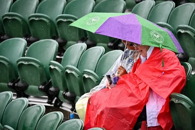 Members of the public wrapped in their rain jackets sit under and umbrella in the stands on court 2 as the tennis matches have been suspended due to the rain on the second day of the 2023 Wimbledon Championships at The All England Tennis Club in Wimbledon, southwest London, on July 4, 2023. (Photo by Glyn Kirk/AFP Photo)