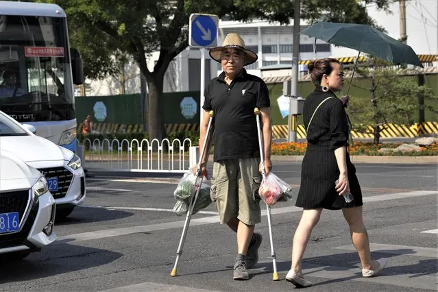 A man on crutches crosses the road with his groceries in Beijing, Monday, July 17, 2023. China's economy grew at a 6.3% annual pace in the April-June quarter, much lower than analysts had forecast given the slow pace of growth the year before. (Photo by Ng Han Guan/AP Photo)