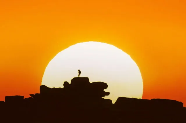 A walker watches a magnificent sunset from Owler Tor, United Kingdom, overlooking the Hope Valley in the Peak District on April 27, 2023. (Photo by Richard Bowring/Animal News Agency)