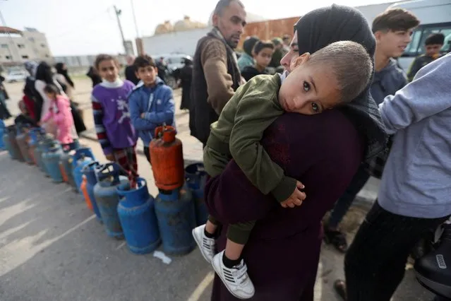 A woman carries a child as Palestinians gather to fill liquid gas cylinders, during a temporary truce between Hamas and Israel, in Rafah in the southern Gaza Strip on November 25, 2023. (Photo by Ibraheem Abu Mustafa/Reuters)