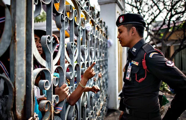 An anti-government demonstrator (L) points his finger at a policeman as they talk through the gate of the Government House in Bangkok on December 12, 2013.  Political turmoil has been rocking the Thai capital for weeks, with protesters seeking to oust Prime Minister Yingluck Shinawatra and rid the kingdom of the influence of her brother, deposed former leader Thaksin. (Photo by Philippe Lopez/AFP Photo)