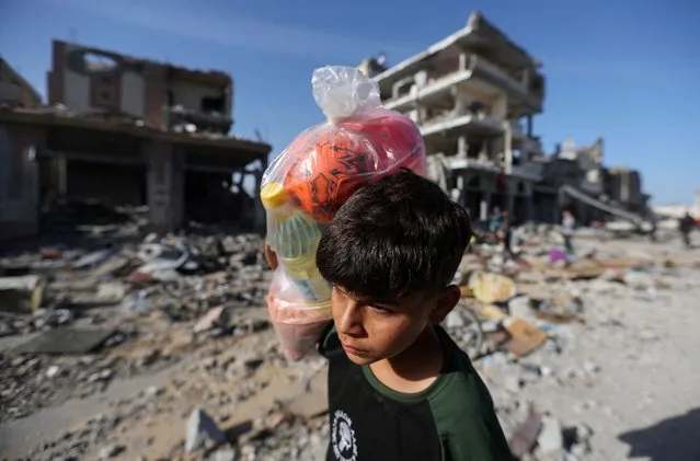 A displaced Palestinian boy carries a bag, as he returns to his home walking next to houses destroyed in an Israeli strike during the conflict, amid the temporary truce between Hamas and Israel, in Khan Younis in the southern Gaza Strip on November 24, 2023. (Photo by Ibraheem Abu Mustafa/Reuters)