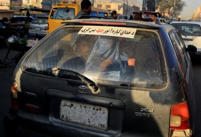 A woman wearing a burqa sits in the trunk of a taxi in Chawok market in Kabul, Afghanistan, October 14, 2021. The sticker reads “for God sake stop fighting”. (Photo by Zohra Bensemra/Reuters)