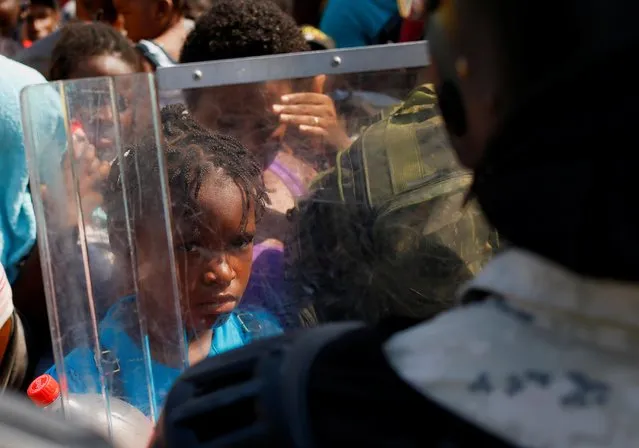 A migrant child is seen through a National Guard member's shield as he and others queue to get on buses after accepting an offer from the Mexican government to obtain humanitarian visas to transit the Mexican territory, at a stadium in Tapachula, Mexico on November 25, 2021. (Photo by Jose Luis Gonzalez/Reuters)