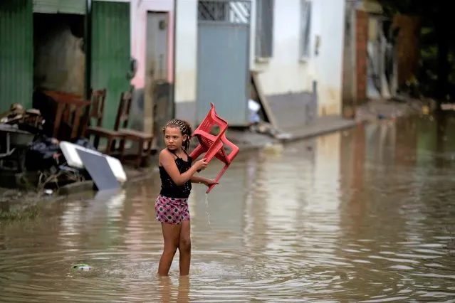 A girl carries a chair in flood waters in Itapetinga, Bahia state, Brazil, Tuesday, December 28, 2021. Two dams broke Sunday in northeastern Brazil, threatening worse flooding in a rain-drenched region that has already seen thousands of forced to flee their homes. (Photo by Raphael Muller/AP Photo)