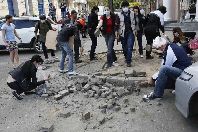 People pull up cobblestones as ammunition during clashes between pro-Russian activists and supporters of the Kiev government in the streets of Odessa May 2, 2014. Police said a man was shot dead in clashes between a crowd backing Kiev and pro-Russian activists in the largely Russian-speaking southern port of Odessa, which lies west of Crimea, annexed by Moscow in March. (Photo by Yevgeny Volokin/Reuters)
