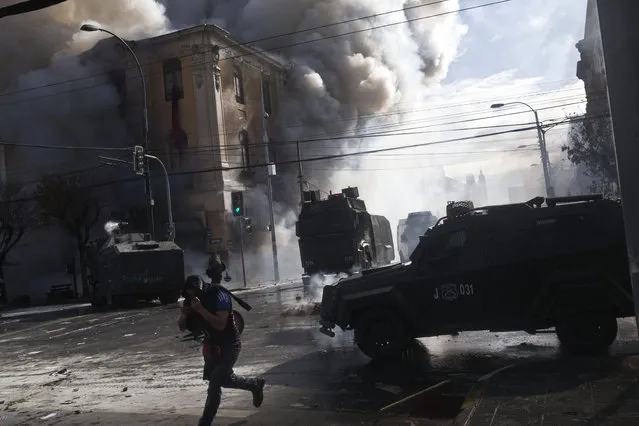A protester runs as anti-riot vehicles approach in an area near Congress, where President Michelle Bachelet was presenting the state-of-the-nation report, in Valparaiso, Chile, Saturday, May 21, 2016. An anti-government protest that began as a peaceful march turned rough as some demonstrators threw rocks at police and gasoline bombs at buildings, resulting in the death of one man who reportedly died of asphyxiation.(AP Photo/Esteban Felix)