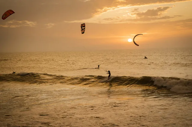 A picture taken on October 10, 2019, shows kitesurfers riding waves at sunset at Dakhla beach in Morocco-administered Western Sahara. In the heart of disputed Western Sahara, a former garrison town has become an unlikely tourist magnet after kitesurfers discovered the windswept desert coast on the Atlantic is perfect for their sport. (Photo by Fadel Senna/AFP Photo)