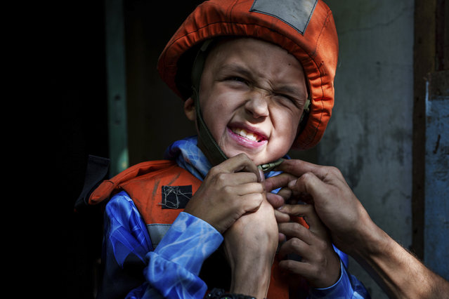 A Fenix team rescue worker places a helmet on Bohdan Scherbyna, 9, as he is evacuated with his mother Maryna Scherbyna and 14 year old sister Angelina Scherbyna, as local people as moved from Selidove to safe areas, in Pokrovsk, Donetsk region, Ukraine, on Tuesday, August 20, 2024. (Photo by Evgeniy Maloletka/AP Photo)