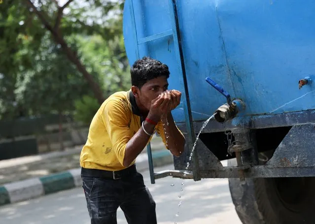 A labourer drinks water from a tanker at a construction site on a hot summer day, in Noida, India, May 12, 2022. (Photo by Anushree Fadnavis/Reuters)
