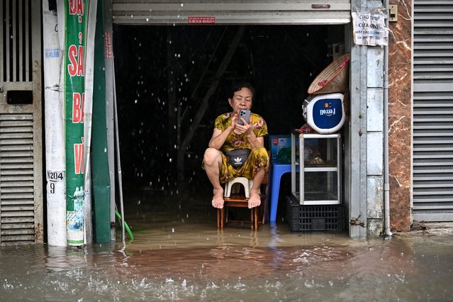 A woman uses a phone while sitting over flood waters at her home in Hanoi on September 11, 2024, as heavy rains in the aftermath of Typhoon Yagi brought flooding to northern Vietnam. Residents of Hanoi waded through waist-deep water on September 11 as river levels hit a 20-year high and the toll from the strongest typhoon in decades passed 150, with neighbouring nations also enduring deadly flooding and landslides. (Photo by Nhac Nguyen/AFP Photo)